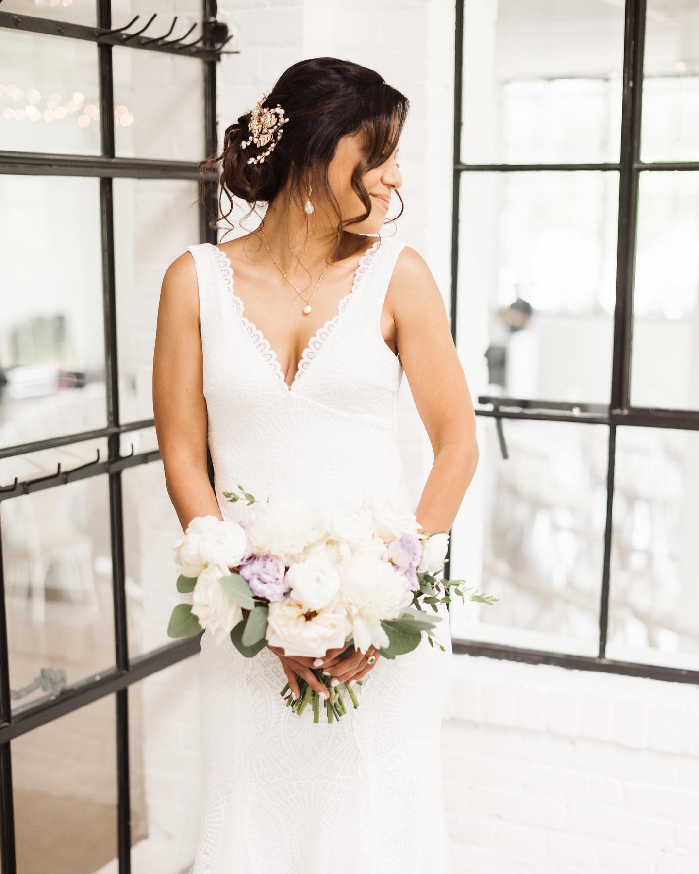 Bride in her wedding gown holding a bouquet beside a bright window