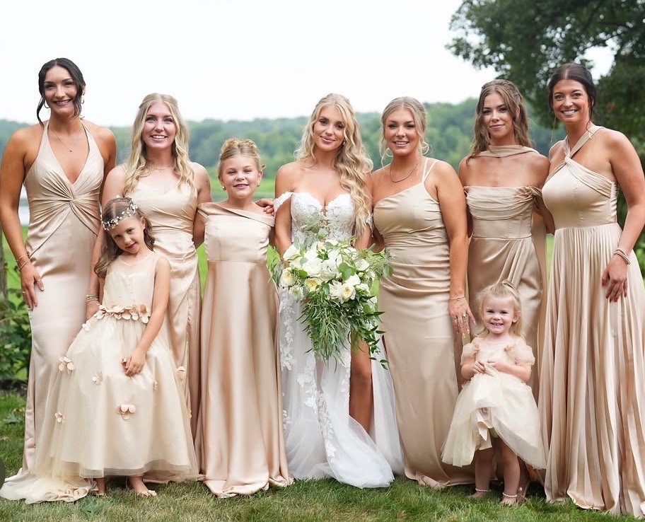 Bride with bridesmaids and two flower girls outdoors near a lake