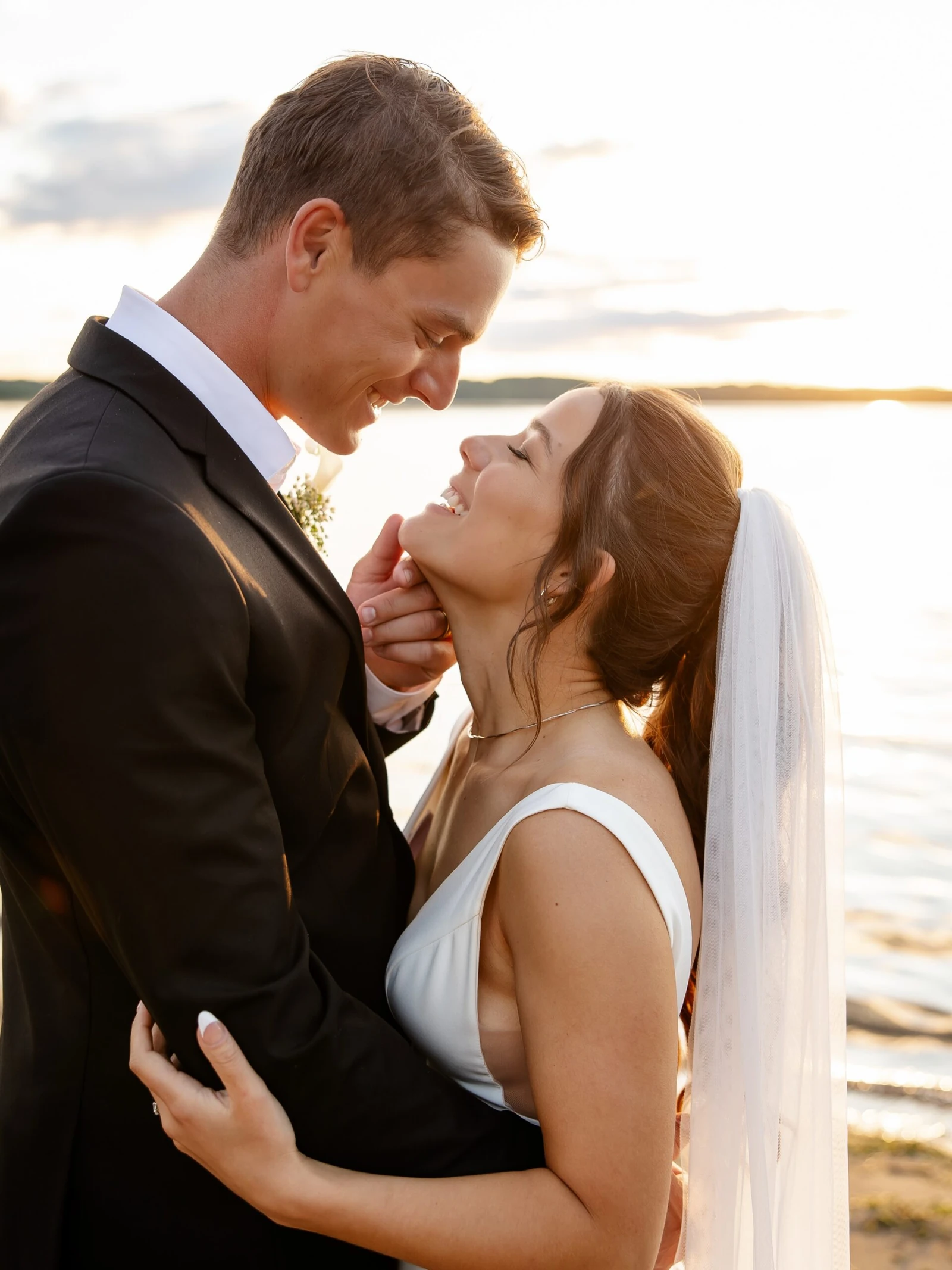 Bride and groom smiling together beside a lake at sunset